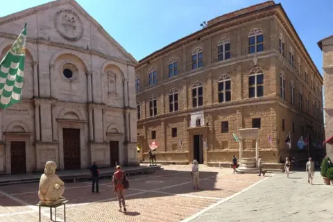 La **Pienza piazza** è un luogo incantevole con un duomo imponente e palazzi rinascimentali. Una scultura e bandiere colorate aggiungono vivacità.