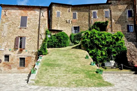 Antico borgo di Monteleone di Roncofreddo, con case in pietra e mattoni, finestre con persiane e un prato verde.
