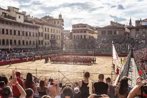 Un campo di sabbia a Firenze, gremito di spettatori, ospita un'intensa partita di calcio storico.