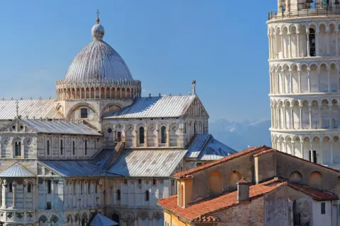 Pisa cosa vedere: il Duomo e la Torre Pendente, capolavori romanici che svettano nel cielo azzurro, con le montagne sullo sfondo.