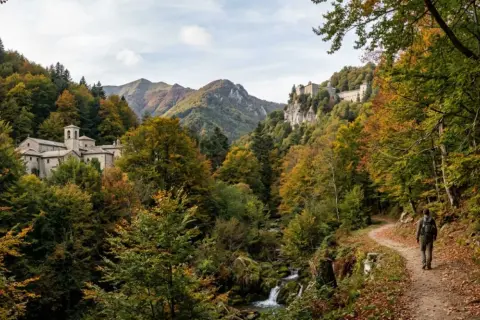 Un escursionista percorre un sentiero tra le Foreste Casentinesi in autunno, con un monastero e un eremo sullo sfondo.