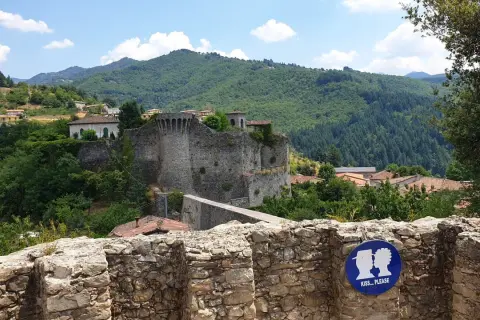 La rocca di Castiglione domina un borgo tra colline verdi. Un cartello invita a baciarsi.