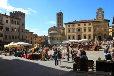 Piazza gremita per l'Arezzo antique market, tra bancarelle di antiquariato e palazzi storici sotto un cielo azzurro.