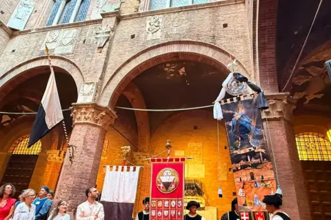 Sfilata storica a Siena con stendardi e costumi d'epoca, evocando l'atmosfera del Palio.