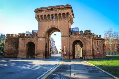 Le imponenti porte di Bologna, con i loro archi in mattoni rossi, accolgono i visitatori sotto un cielo azzurro.
