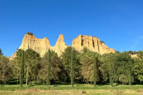 Le maestose balze del Valdarno si stagliano contro un cielo azzurro, circondate da una rigogliosa vegetazione e cipressi slanciati.