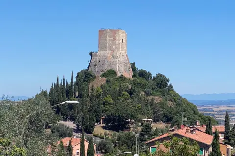 La rocca di Tentennano domina il paesaggio collinare toscano, circondata da cipressi e case con tetti rossi.