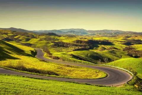 Strada volterrana serpeggia tra dolci colline verdi, un invito a esplorare paesaggi mozzafiato sotto un cielo limpido.