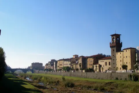 Pescia: cosa vedere? Un fiume serpeggia tra edifici storici e una torre imponente, sotto un cielo azzurro.