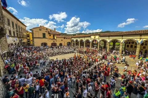 Folla in piazza per il palio dei rioni Castiglion Fiorentino, con figuranti in costume e bandiere.
