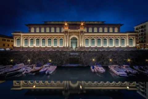 Il mercato di Livorno illuminato di notte, con barche ormeggiate e il loro riflesso sull'acqua.