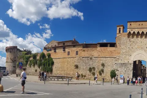 La **Siena Fortezza Medicea** domina il paesaggio con le sue mura imponenti. Turisti passeggiano sotto il sole, ammirando la storia.
