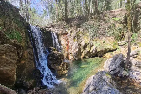 Cascata nel bosco, acque cristalline del fiume Merse che scendono tra rocce e vegetazione lussureggiante.