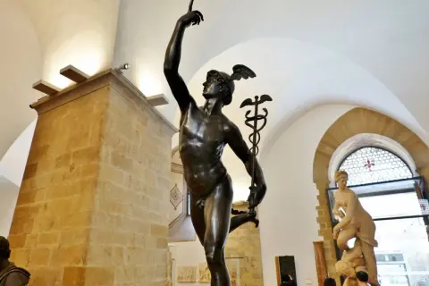 Mercurio in bronzo, un'opera che ricorda la grazia del David di Donatello. La statua, con il suo elmo alato, si staglia contro un soffitto ad arco.