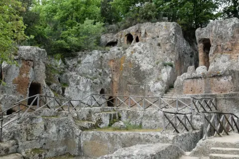 Antiche tombe scavate nella roccia, parte di siti etruschi, con sentieri e recinzioni in legno.