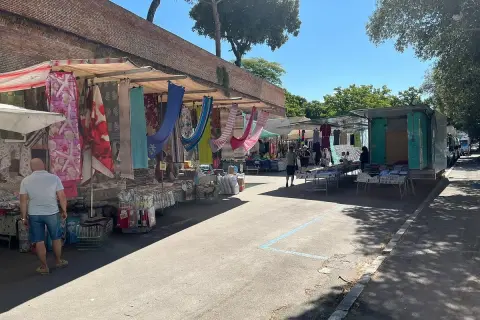 Mercato all'aperto a Grosseto, con bancarelle colorate di tessuti e abbigliamento sotto un cielo azzurro.