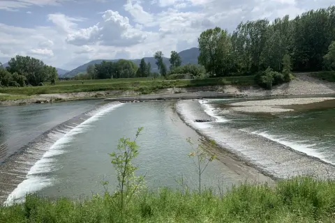 Il **parco fluviale del Serchio** offre uno spettacolo di acqua che scorre su dighe naturali, circondato da verdi colline e alberi rigogliosi sotto un cielo nuvoloso.