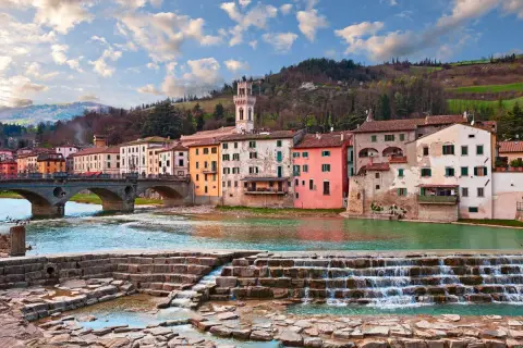 Il **parco fluviale Santa Sofia** con case colorate affacciate sul fiume e un ponte ad archi.