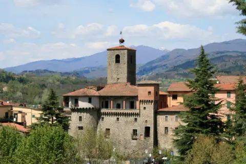 La Rocca Ariostesca domina il borgo con la sua torre imponente, circondata da case dai tetti rossi e verdi colline.