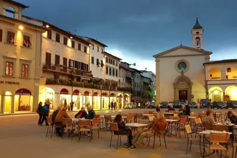 Piazza serale con tavolini all'aperto e una chiesa, un'atmosfera incantevole nei borghi da visitare vicino a Figline Valdarno.