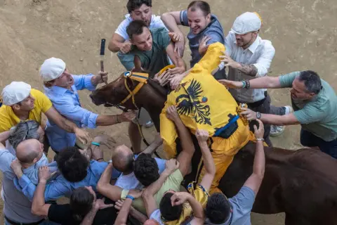 Caos e passione al Palio di Siena: uomini lottano per il cavallo, mostrando l'intensità delle regole non scritte di questa storica corsa.