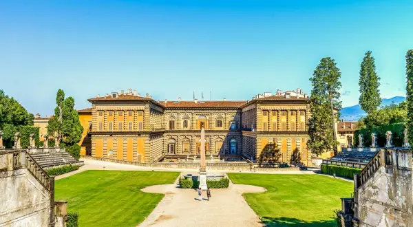 Il maestoso Palazzo Pitti si staglia contro un cielo azzurro, circondato da giardini lussureggianti e antiche scalinate.