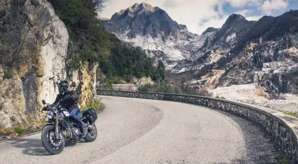 Motociclista su strada tortuosa con montagne di marmo sullo sfondo. Perfetto per itinerari moto Toscana 3 giorni.