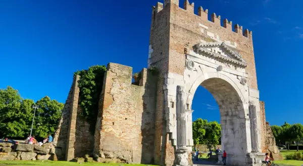 L'imponente arco augusto rimini, con la sua antica pietra e la torre in mattoni, si staglia contro un cielo azzurro.