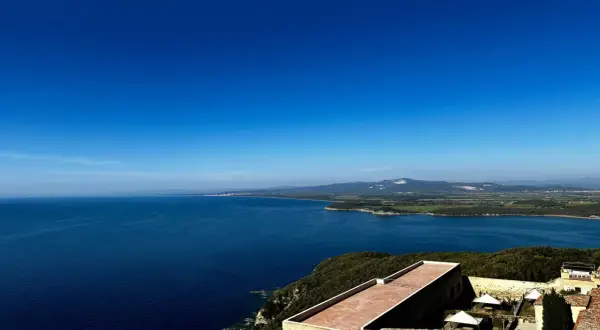 Vista panoramica sul mare blu intenso della Maremma, con colline verdi e un borgo antico. Perfetto per scoprire cosa vedere in Maremma.
