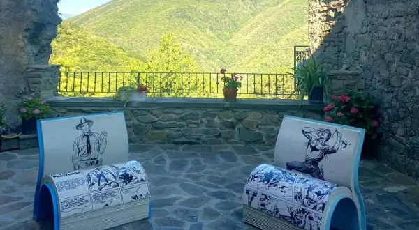 Due sedie a forma di libro con fumetti western, in un cortile con vista sulle colline verdi. Montereggio, paese dei librai, offre un angolo lettura unico.