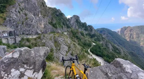 Bicicletta gialla in primo piano, con un panorama mozzafiato di montagne scoscese e un passo del vestito che si snoda tra le rocce.