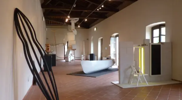 Interno del **mudac carrara** con sculture moderne, tra cui una grande forma nera appoggiata al muro e una barca bianca al centro.