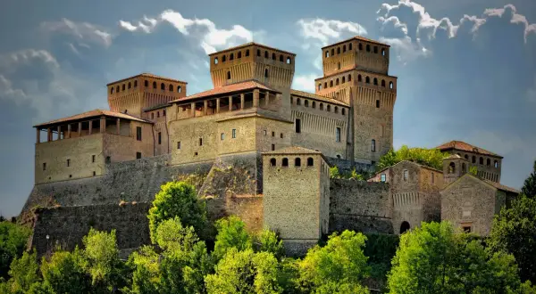 Rocche imponenti e torri medievali, tra i borghi vicino Parma, si stagliano contro un cielo nuvoloso, circondate da un verde lussureggiante.