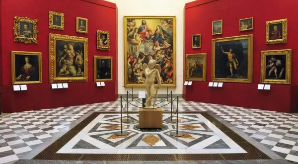 Sala con opere d'arte nei musei d'arte a Firenze. Statua di Cupido al centro, circondata da dipinti su pareti rosse.