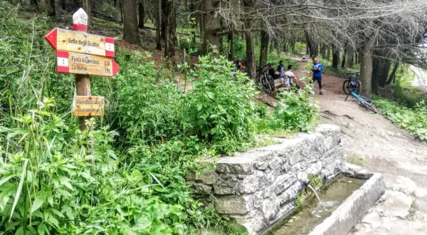 Segnavia per il trekking sul Monte Morello, con ciclisti che riposano vicino a una fontana.