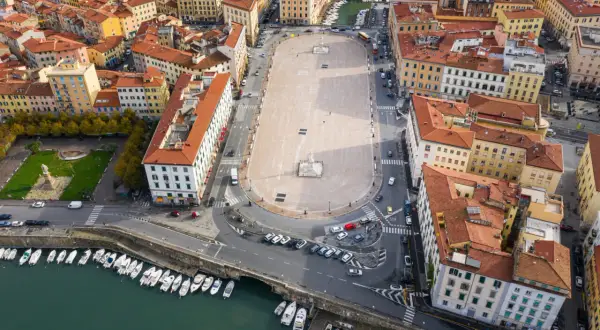 Vista aerea della piazza della Repubblica a Livorno, con edifici storici, un monumento centrale e barche ormeggiate nel canale.
