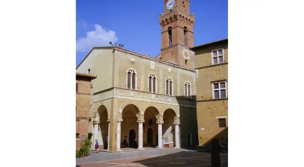Il **Palazzo Comunale di Pienza** domina la piazza con la sua torre dell'orologio. Archi eleganti e finestre gotiche caratterizzano l'edificio.