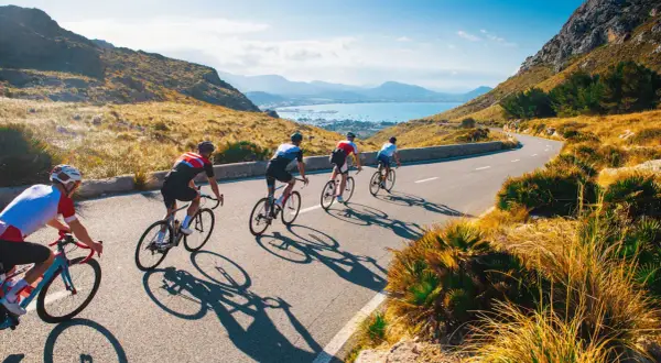 Ciclisti su strada panoramica, ideali per itinerari bici 3 giorni. Paesaggio montuoso e mare sullo sfondo.