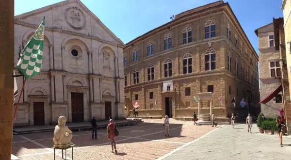 La **Pienza piazza** è un luogo incantevole con un duomo imponente e palazzi rinascimentali. Una scultura e bandiere colorate aggiungono vivacità.