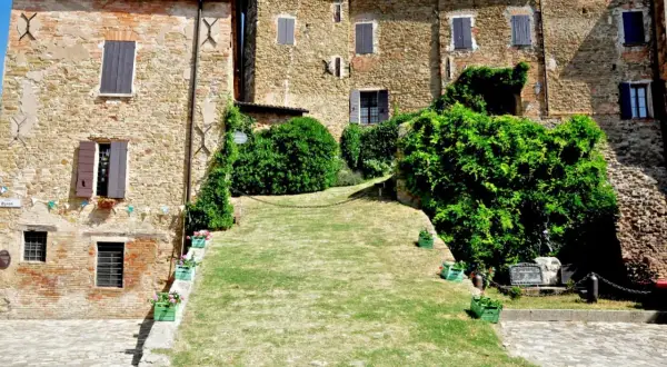 Antico borgo di Monteleone di Roncofreddo, con case in pietra e mattoni, finestre con persiane e un prato verde.