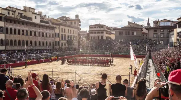 Un campo di sabbia a Firenze, gremito di spettatori, ospita un'intensa partita di calcio storico.