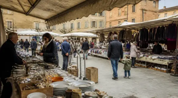 Gente al montepulciano markt, tra bancarelle di abiti e stoviglie, in una piazza storica.