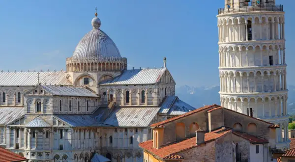 Pisa cosa vedere: il Duomo e la Torre Pendente, capolavori romanici che svettano nel cielo azzurro, con le montagne sullo sfondo.