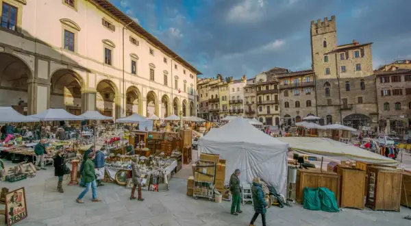 Mercato all'aperto a San Gimignano, con bancarelle di antiquariato e artigianato sotto un cielo nuvoloso.