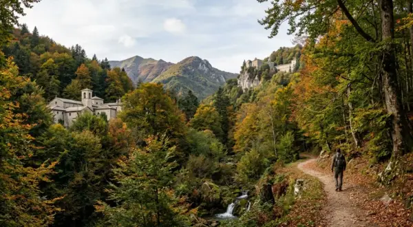 Un escursionista percorre un sentiero tra le Foreste Casentinesi in autunno, con un monastero e un eremo sullo sfondo.