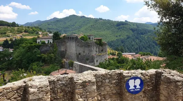 La rocca di Castiglione domina un borgo tra colline verdi. Un cartello invita a baciarsi.