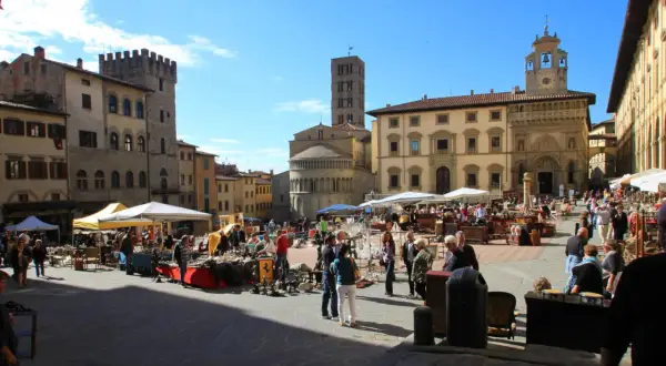 Piazza gremita per l'Arezzo antique market, tra bancarelle di antiquariato e palazzi storici sotto un cielo azzurro.