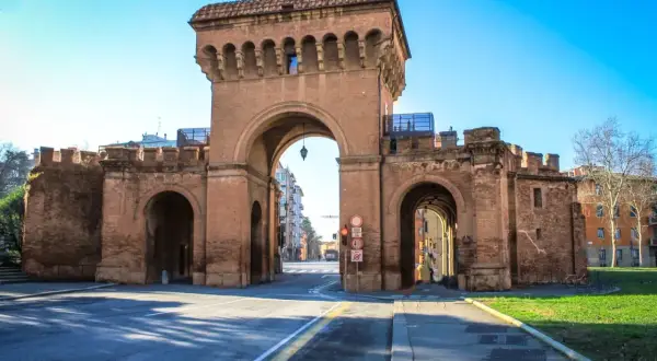 Le imponenti porte di Bologna, con i loro archi in mattoni rossi, accolgono i visitatori sotto un cielo azzurro.