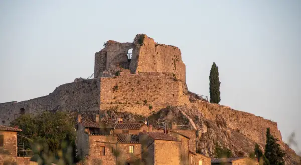 Rocca Aldobrandesca a Castiglione d'Orcia, un antico maniero in pietra che domina il borgo, con un cipresso solitario a vegliare.