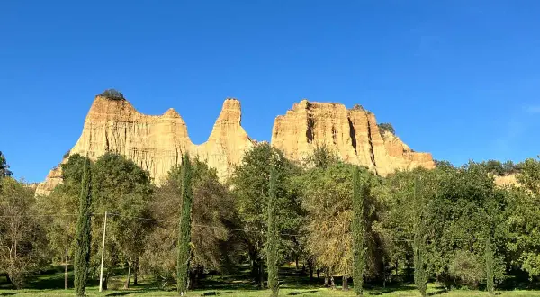 Le maestose balze del Valdarno si stagliano contro un cielo azzurro, circondate da una rigogliosa vegetazione e cipressi slanciati.